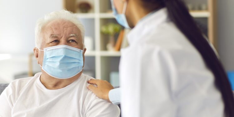 Ärztin und älterer Patient mit Mund-Nasen-Schutz