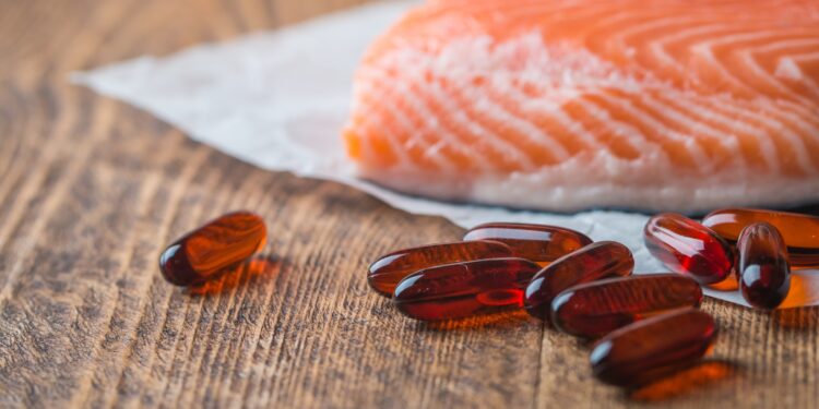 Tabletki Omega-3 i kawałek łososia na drewnianej powierzchni.