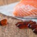 Omega-3-Pillen und ein Stück Lachs liegen auf einer hölzernen Oberfläche.