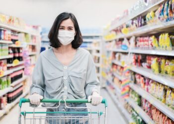 Frau mit Mund-Nasen-Schutz mit Einkaufswagen im Supermarkt