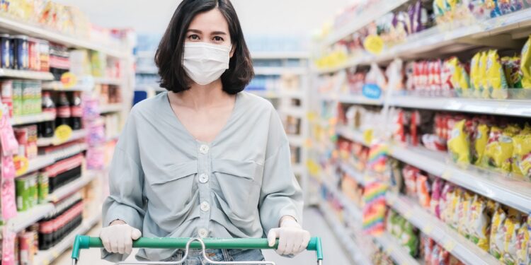 Frau mit Mund-Nasen-Schutz mit Einkaufswagen im Supermarkt