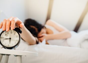 Eine Frau macht im Halbschlaf ihren Wecker aus.