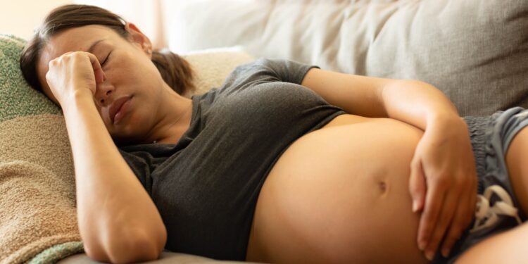 Schwangere Frau liegt auf dem Sofa und fast sich an den Kopf.