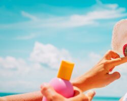 Frau cremt Mädchen mit Sonnenhut und Sonnenbrille das Gesicht mit Sonnenschutzcreme ein.