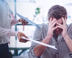 Gestresster Mann am Computer, dem von allen Seiten Unterlagen gereicht werden.