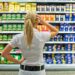 Eine Frau steht mit nachdenklicher Körperhaltung vor einem Regal im Supermarkt.