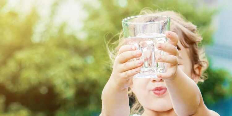 Mädchen hält mit beiden Händen ein Wasserglas nach oben