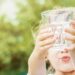 Mädchen hält mit beiden Händen ein Wasserglas nach oben