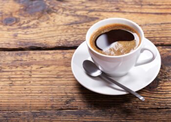 Eine Tasse schwarzer Kaffee mit einem Löffel auf einem Holztisch
