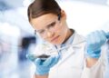 Eine Frau in Laborkleidung gibt mit einer Pipette eine Flüssigkeit in eine Petrischale.