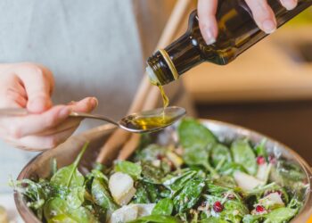 Frau gibt Speiseöl zu einem Salat