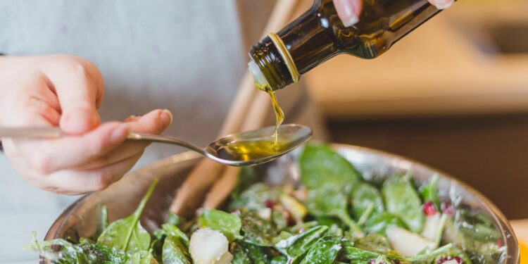 Frau gibt Speiseöl zu einem Salat