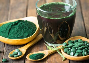 Dunkelgrüner Extrakt aus der Spirulina-Alge als Getränk, Pulver und Kapseln auf Holztisch