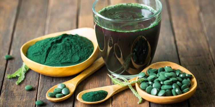 Dunkelgrüner Extrakt aus der Spirulina-Alge als Getränk, Pulver und Kapseln auf Holztisch