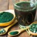 Dunkelgrüner Extrakt aus der Spirulina-Alge als Getränk, Pulver und Kapseln auf Holztisch