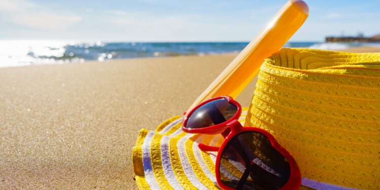 Ein Hut, eine Sonnenbrille und Sonnencreme liegen auf einem Strand.