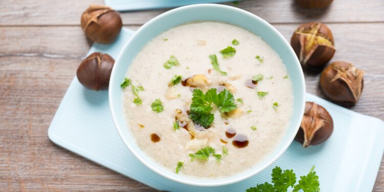 Esskastanien-Creme-Suppe in weißer Suppenschüssel, daneben einige Esskastanien