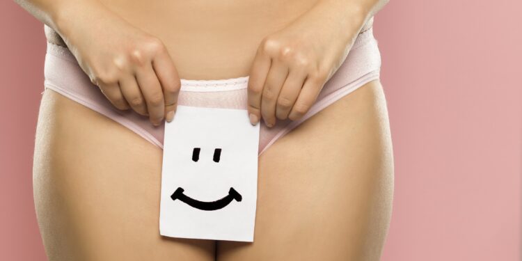 Eine Frau hält ein Papier mit einem Smiley vor ihre Unterwäsche.