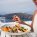 Restaurant woman eating salad luxury europe travel Santorini vacation. Healthy lifestyle people relaxing on Greece holidays.