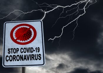 Auf einem Schild steht "STOP COVID-19". Im Hintergrund tobt ein Gewitter.