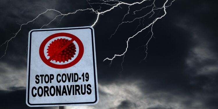 Auf einem Schild steht "STOP COVID-19". Im Hintergrund tobt ein Gewitter.