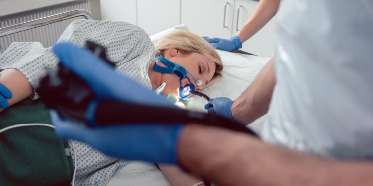 Arzt führt die Kamera von Gastroskop in Mund von Patientin ein
