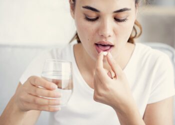 Junge Frau nimmt eine Tablette mit einem Glas Wasser ein
