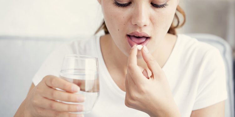 Junge Frau nimmt eine Tablette mit einem Glas Wasser ein