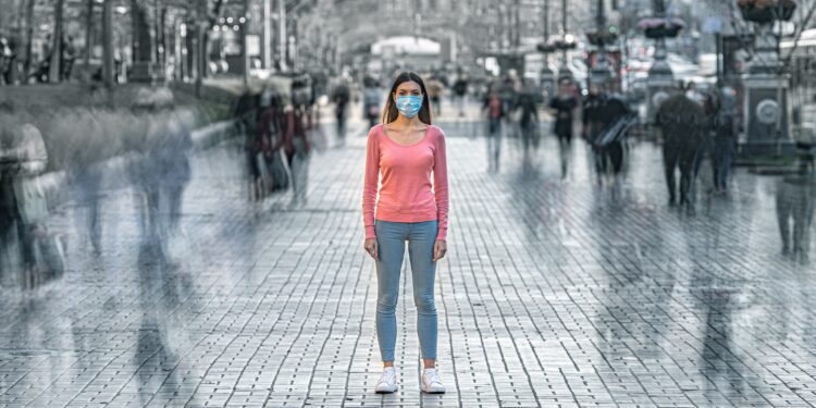 Junge Frau mit medizinischer Maske steht allein im Freien