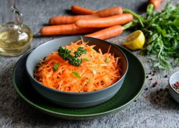 Eine Schale mit Karottensalat steht auf einer Oberfläche.