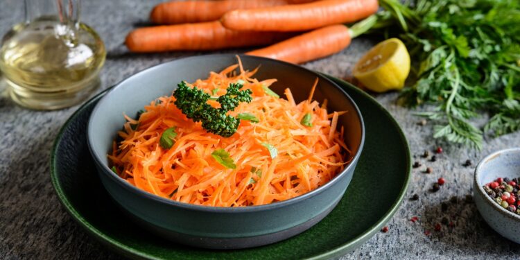 Eine Schale mit Karottensalat steht auf einer Oberfläche.