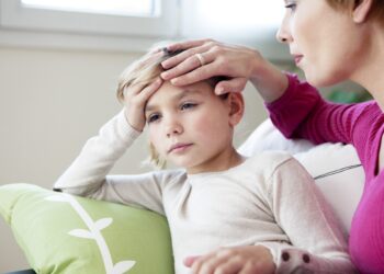 Mutter legt Hand auf die Stirn ihrer kranken Tochter