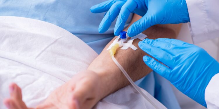 Männlicher Patient mit Kanüle für Bluttransfusion im Arm im Krankenhausbett