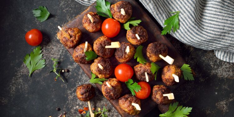 Fleischbällchen und Tomaten sind auf einer hölzernen Platte angerichtet.