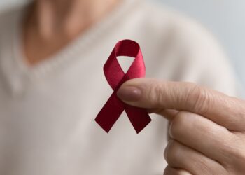 Weibliche Hand mit einer roten Schleife, dem Aids-Bewusstseinssymbol