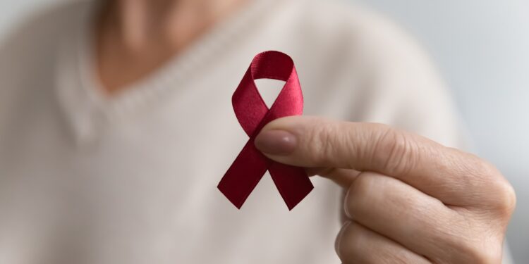 Weibliche Hand mit einer roten Schleife, dem Aids-Bewusstseinssymbol