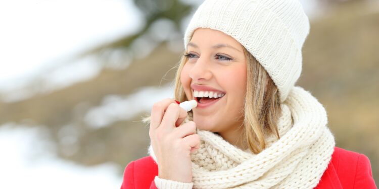 Junge Frau schützt ihrer Lippen mit Lippenbalsam vor der Kälte