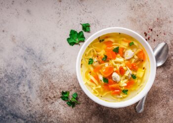 Eine Schüssel mit Hühner-Nudelsuppe steht auf einer hellen Oberfläche.