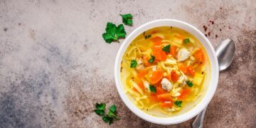 Eine Schüssel mit Hühner-Nudelsuppe steht auf einer hellen Oberfläche.