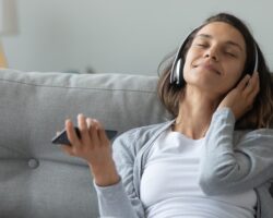 Junge Frau mit Kopfhörer sitzt auf dem Sofa und entspannt mit Musik