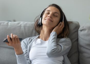 Junge Frau mit Kopfhörer sitzt auf dem Sofa und entspannt mit Musik