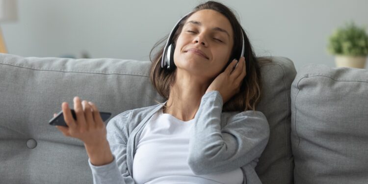 Junge Frau mit Kopfhörer sitzt auf dem Sofa und entspannt mit Musik