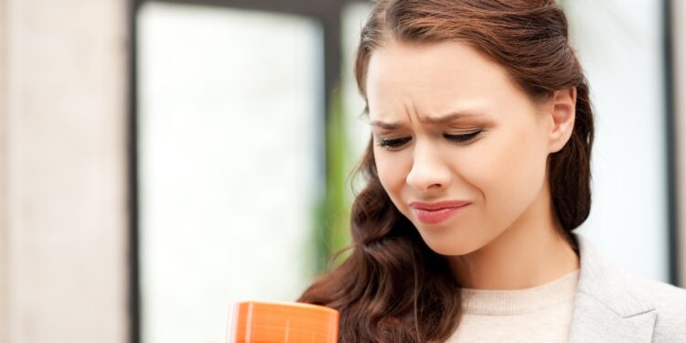 Eine Frau mit einer Kaffeetasse in der Hand verzieht das Gesicht.