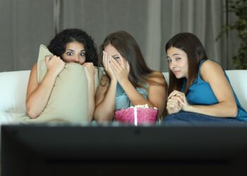 Drei junge Frauen sitzen ängstlich auf de, Sofa und sehen einen Horrorfilm