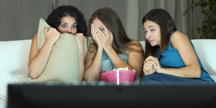 Drei junge Frauen sitzen ängstlich auf de, Sofa und sehen einen Horrorfilm