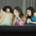 Drei junge Frauen sitzen ängstlich auf de, Sofa und sehen einen Horrorfilm