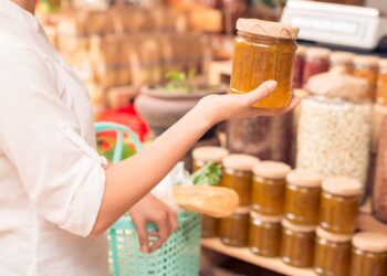 Eine Frau im Supermarkt hält ein Glas Marmelade in der Hand.