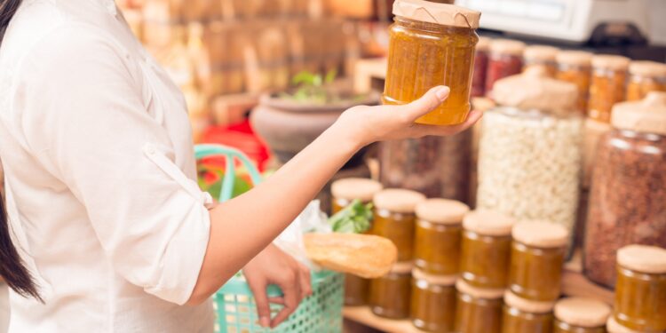 Eine Frau im Supermarkt hält ein Glas Marmelade in der Hand.