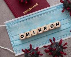 Würfel mit Buchstaben, die das Wort "OMIKRON" bilden, liegen auf einer Mund-Nasen-Schutzmaske.