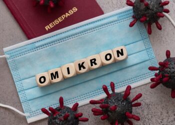 Würfel mit Buchstaben, die das Wort "OMIKRON" bilden, liegen auf einer Mund-Nasen-Schutzmaske.